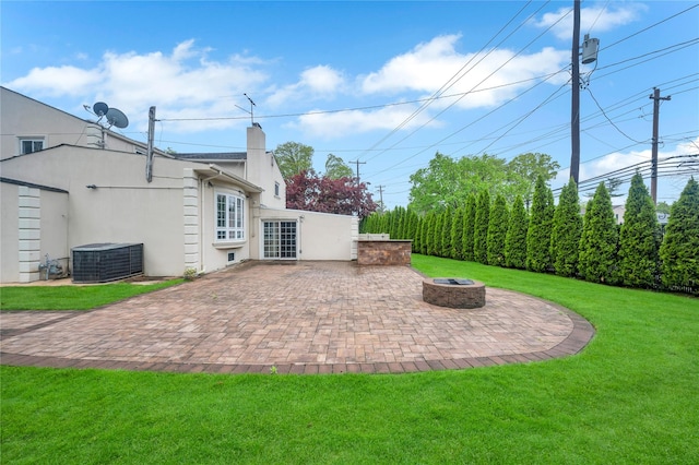 rear view of house featuring central AC, a patio, a fire pit, and a lawn