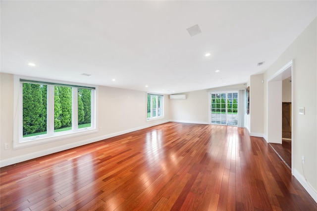 unfurnished living room featuring a wall mounted air conditioner, baseboards, and hardwood / wood-style flooring