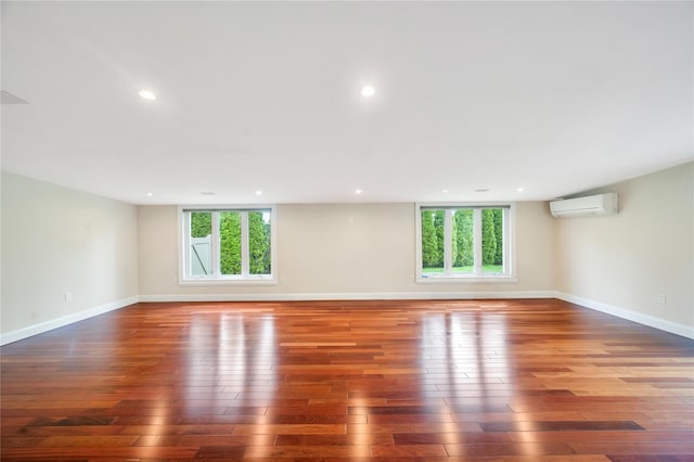 empty room featuring hardwood / wood-style floors, an AC wall unit, baseboards, and recessed lighting