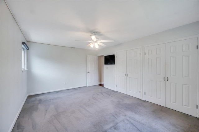 unfurnished bedroom featuring two closets, carpet, baseboards, and ceiling fan