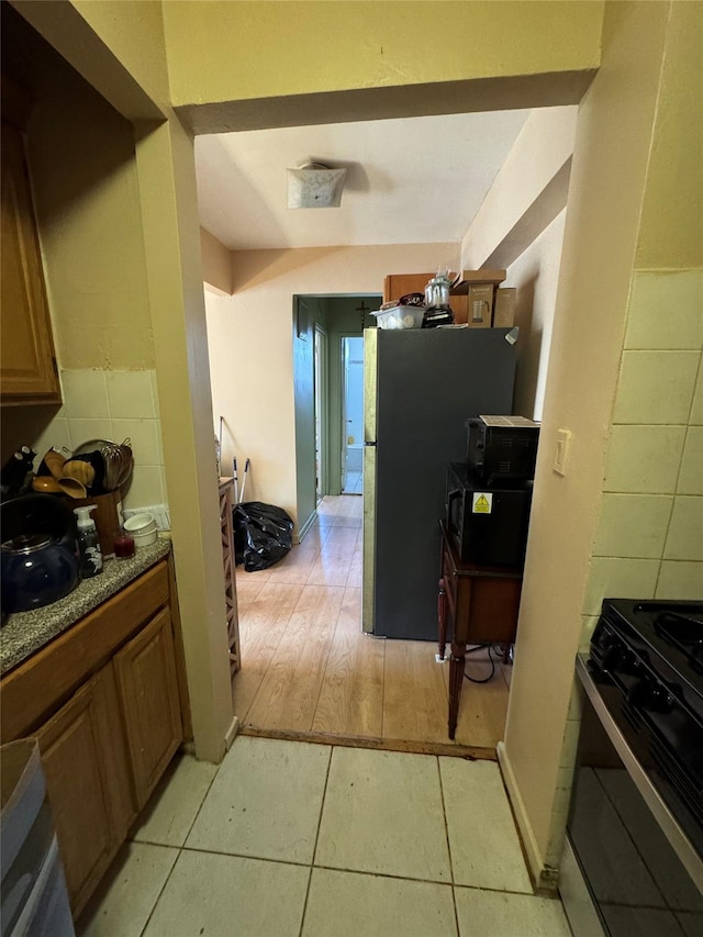 kitchen with light tile patterned floors, freestanding refrigerator, brown cabinets, and gas range oven