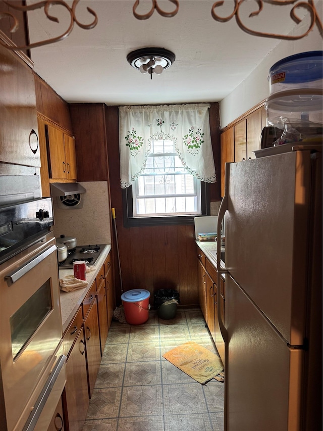 1171 Leland Ave, Bronx, NY 10472 - kitchen with freestanding refrigerator, wall oven, light flooring, wood walls, and brown cabinets