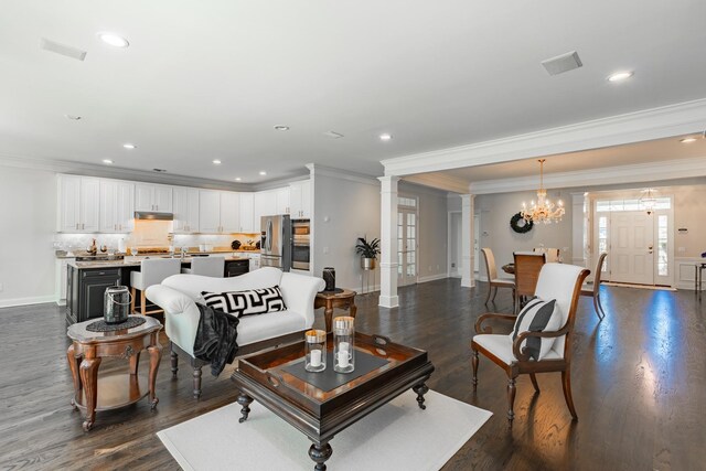 living room with an inviting chandelier, ornamental molding, baseboards, decorative columns, and dark wood-style floors