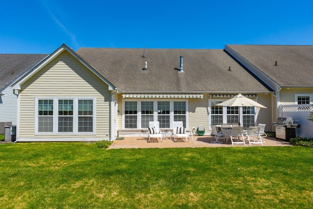 back of property featuring a patio, a shingled roof, and a yard