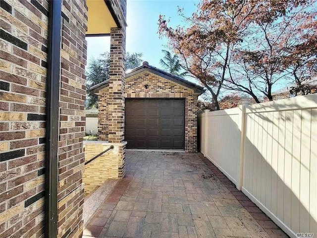 view of side of property featuring fence, an outbuilding, an attached garage, and brick siding
