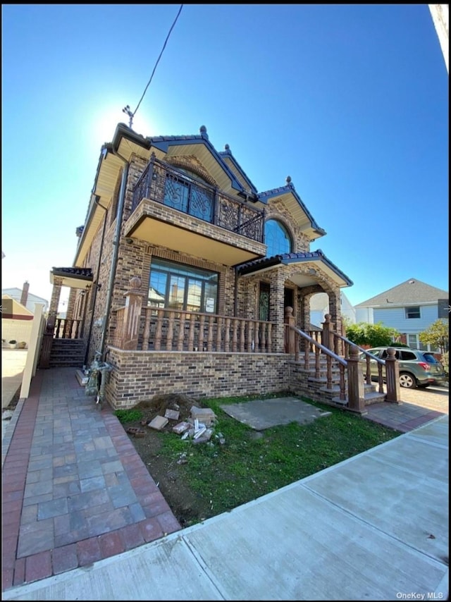 view of front facade featuring a porch, brick siding, and a balcony