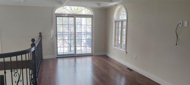interior space with visible vents, access to exterior, dark wood finished floors, beam ceiling, and baseboards