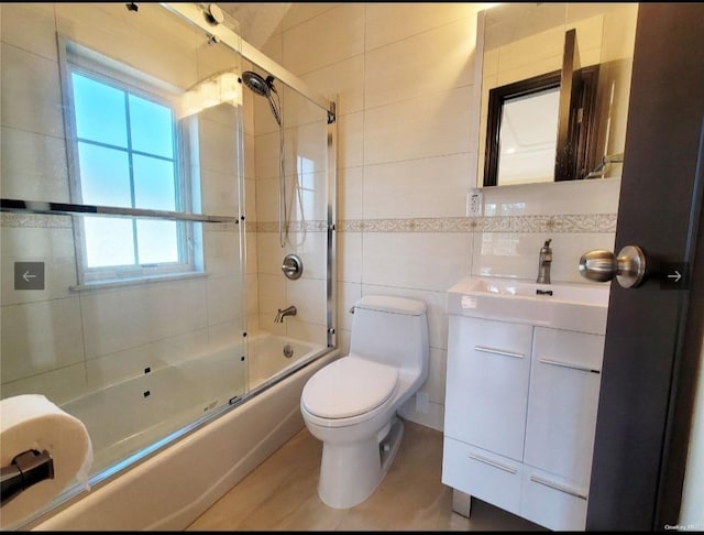 full bath with tile walls, plenty of natural light, bath / shower combo with glass door, and vanity