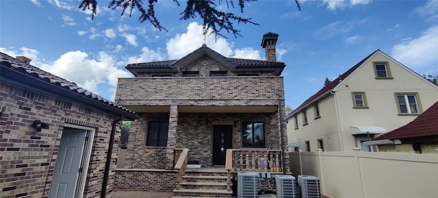 rear view of property featuring fence, brick siding, a porch, a chimney, and cooling unit