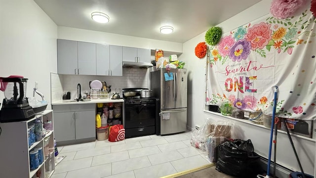 kitchen featuring black gas range, freestanding refrigerator, under cabinet range hood, a sink, and gray cabinetry