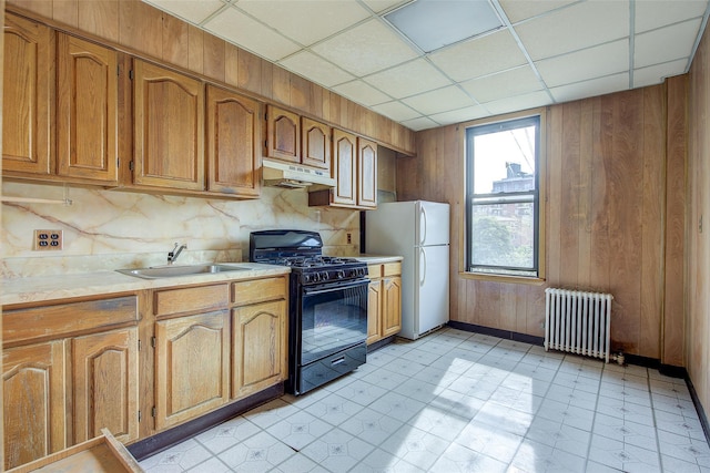 kitchen featuring light countertops, a sink, black gas range oven, radiator heating unit, and under cabinet range hood