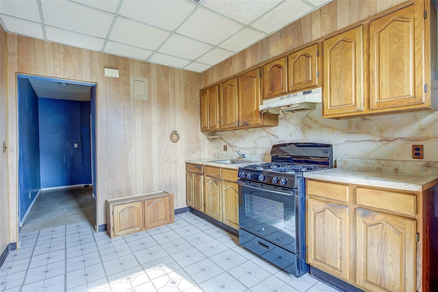 kitchen featuring wood walls, gas stove, light countertops, a sink, and under cabinet range hood