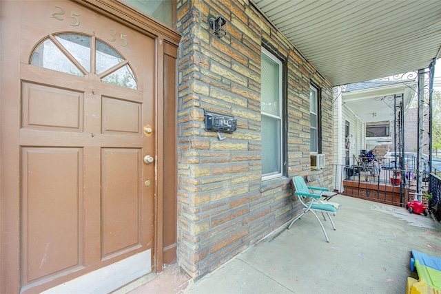 property entrance featuring a porch, stone siding, and cooling unit