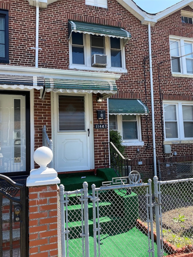 doorway to property with brick siding, a gate, fence, and cooling unit