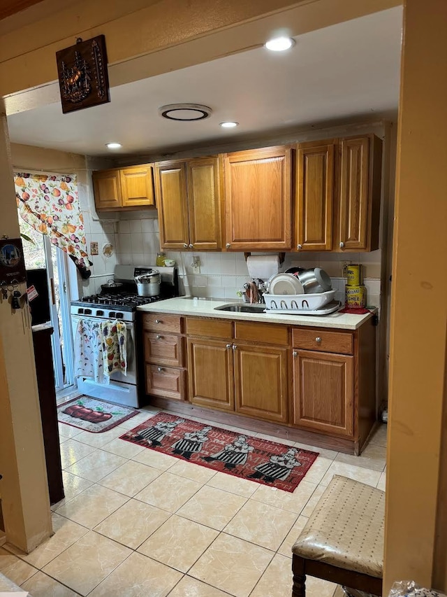 kitchen with stainless steel gas range, brown cabinets, light tile patterned flooring, and light countertops