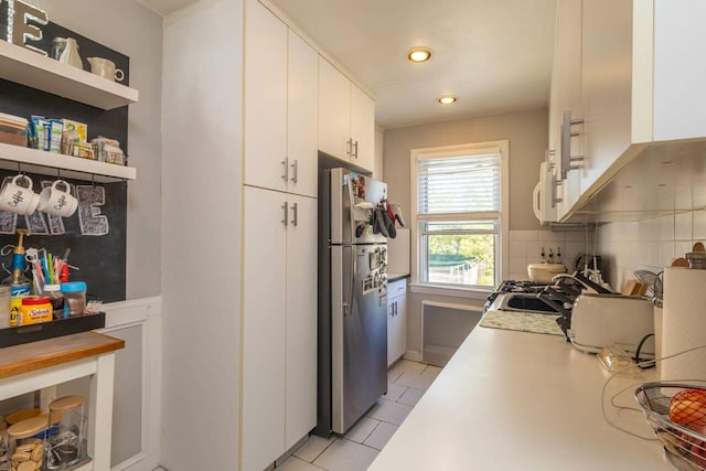 kitchen with light countertops, white cabinets, freestanding refrigerator, white microwave, and light tile patterned flooring