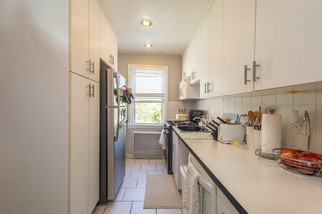 kitchen featuring light countertops, light tile patterned floors, white cabinets, appliances with stainless steel finishes, and backsplash