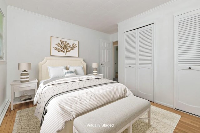 900 Cedar Dr, Southold, NY 11971 - bedroom featuring light wood finished floors, crown molding, multiple closets, baseboard heating, and baseboards