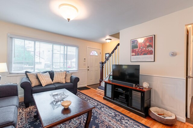 living room featuring plenty of natural light, wood finished floors, wainscoting, stairway, and a decorative wall