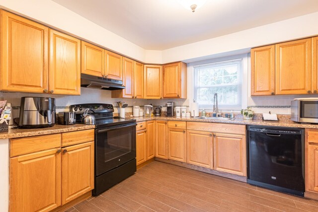 kitchen with black appliances, under cabinet range hood, a sink, light wood-type flooring, and light stone counters