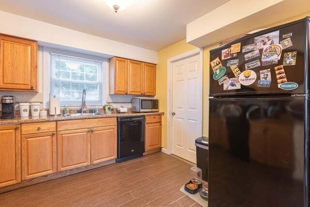 kitchen featuring black appliances, a sink, wood finished floors, and stone counters