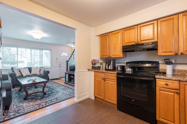 kitchen with black range with electric cooktop, under cabinet range hood, dark wood-type flooring, open floor plan, and a wainscoted wall