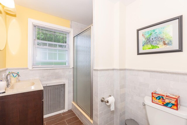 full bathroom with tile walls, toilet, a shower stall, vanity, and a wainscoted wall