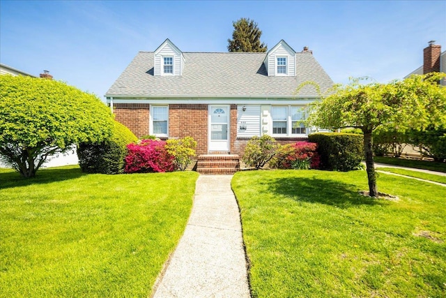 cape cod-style house with a shingled roof, a chimney, brick siding, and a front yard