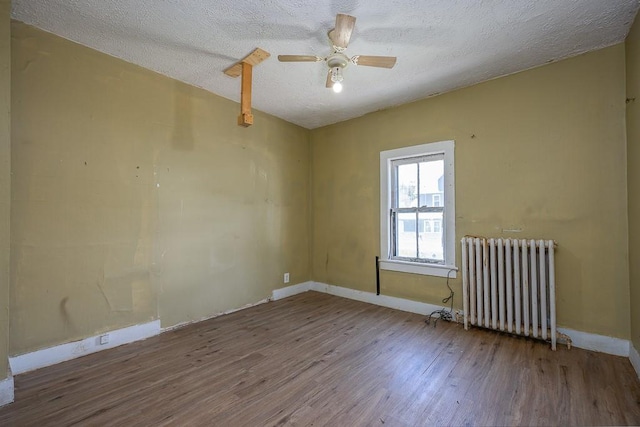 spare room with radiator, wood finished floors, baseboards, ceiling fan, and a textured ceiling