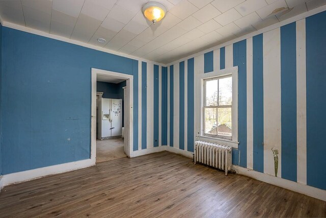 spare room with radiator heating unit, baseboards, crown molding, and hardwood / wood-style floors