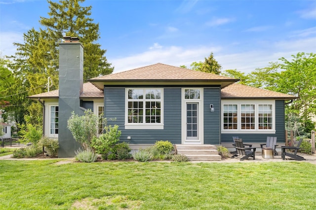 back of property with a chimney, a yard, and roof with shingles