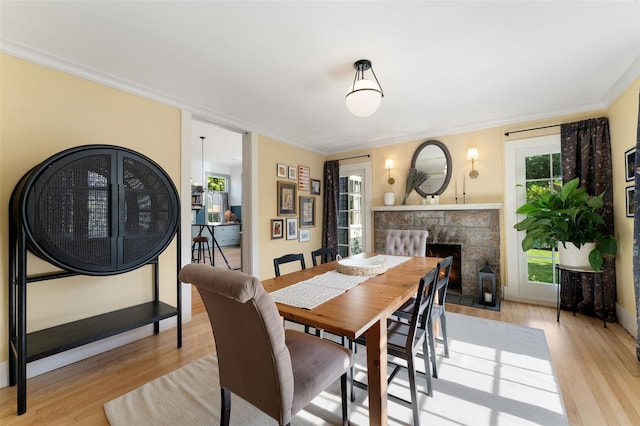 dining space with light wood-type flooring, a fireplace, and ornamental molding