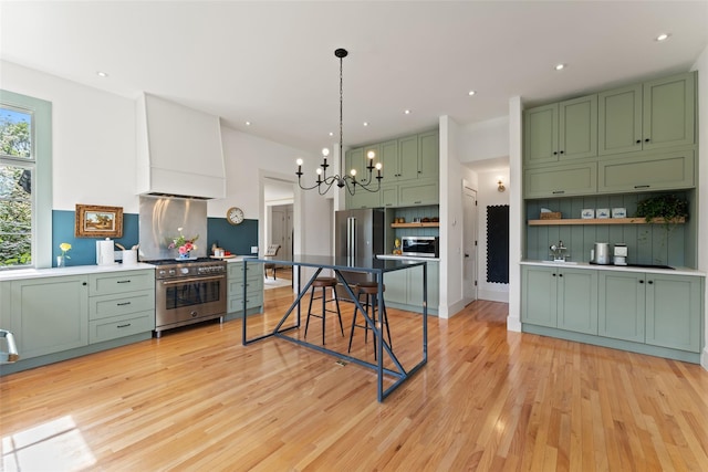 kitchen featuring green cabinets, stainless steel appliances, a chandelier, light wood-style flooring, and decorative light fixtures