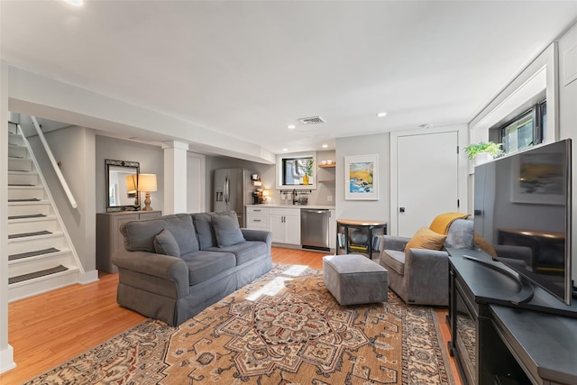 living area with light wood-style flooring, stairs, recessed lighting, and bar area