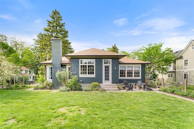 rear view of property with a chimney, a yard, a patio, and a shingled roof