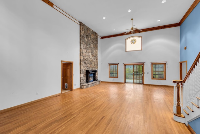 unfurnished living room featuring crown molding, a high ceiling, stairway, light wood-type flooring, and a ceiling fan