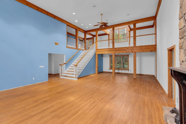 unfurnished living room featuring stairs, wood finished floors, ceiling fan, a high ceiling, and plenty of natural light
