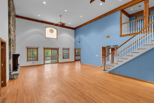 unfurnished living room featuring ceiling fan, a stone fireplace, stairway, and a towering ceiling