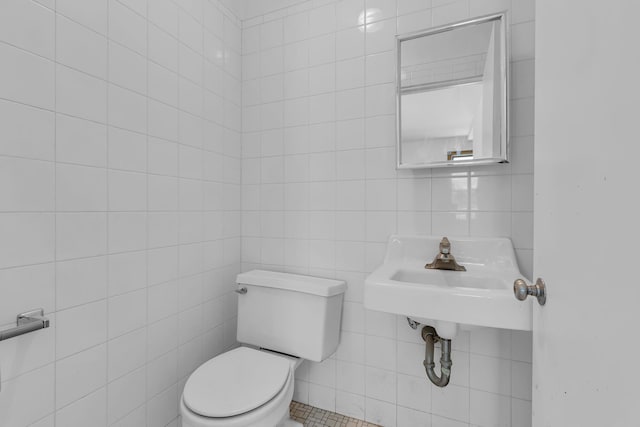 half bath with toilet, tile walls, and a sink