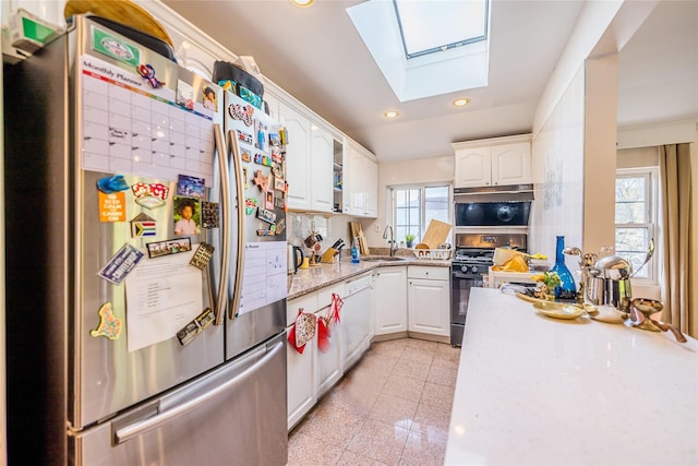 kitchen featuring range with gas stovetop, freestanding refrigerator, recessed lighting, white cabinetry, and a skylight