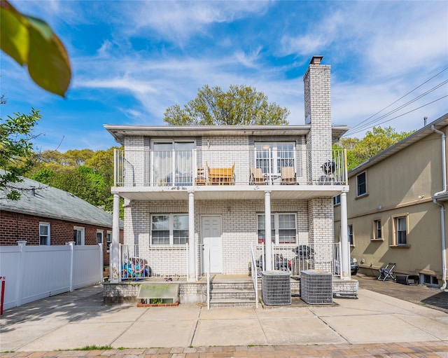 rear view of house with fence, covered porch, brick siding, and a balcony