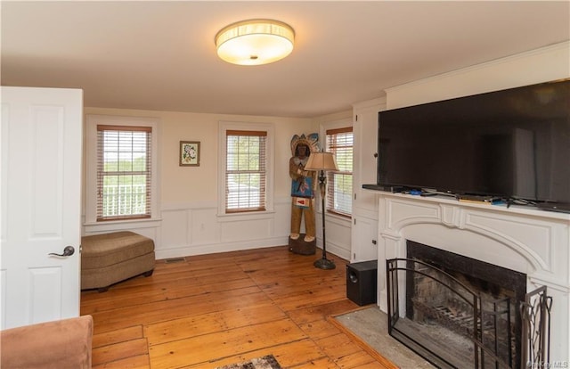 living area featuring a fireplace with flush hearth, wainscoting, light wood-style flooring, and a healthy amount of sunlight