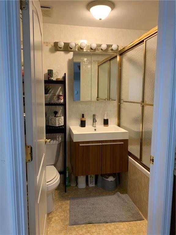 bathroom featuring vanity, backsplash, combined bath / shower with glass door, and toilet