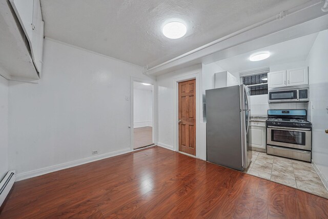 1754 Seward Ave, Bronx, NY 10473 - kitchen with white cabinetry, baseboards, a baseboard radiator, stainless steel appliances, and light wood-style flooring