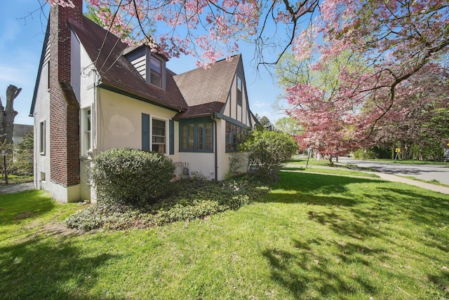 view of side of home with a lawn, roof with shingles, stucco siding, and a chimney