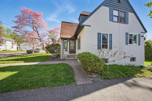 view of front facade featuring a shingled roof, a front lawn, and stucco siding