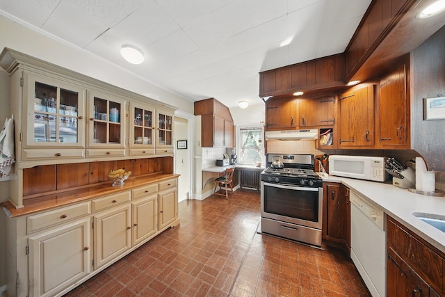 kitchen with light countertops, under cabinet range hood, brick patterned floor, and white appliances