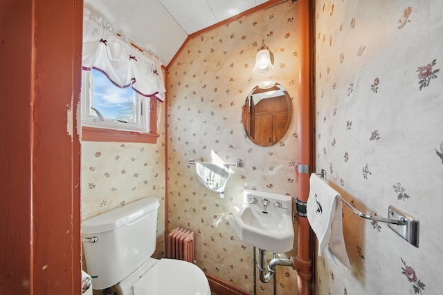 half bathroom featuring a sink, toilet, radiator heating unit, baseboards, and wallpapered walls