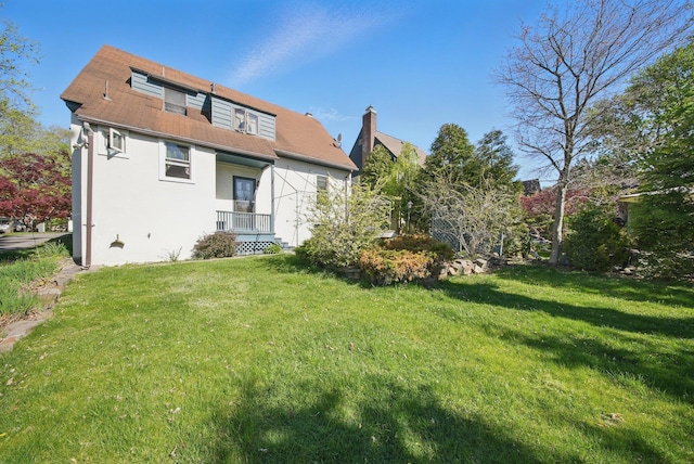 rear view of property featuring a shingled roof, stucco siding, and a yard