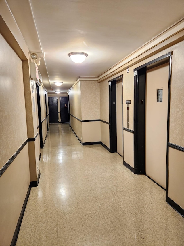 hallway with baseboards, elevator, and light floors
